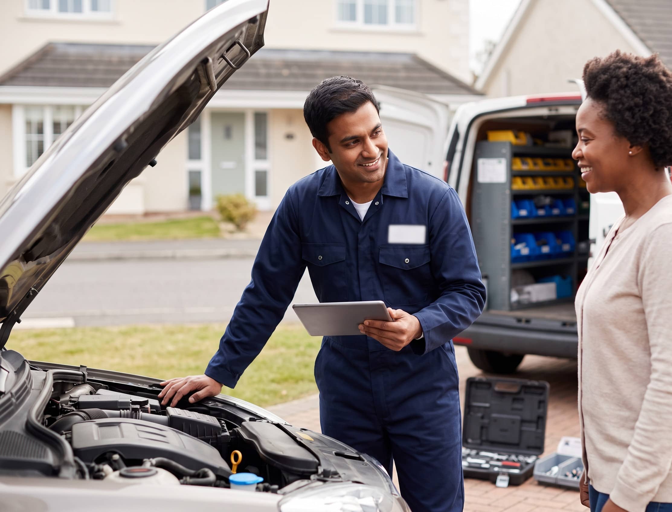 A mobile technician working at a customer’s car in their driveway, service van behind
